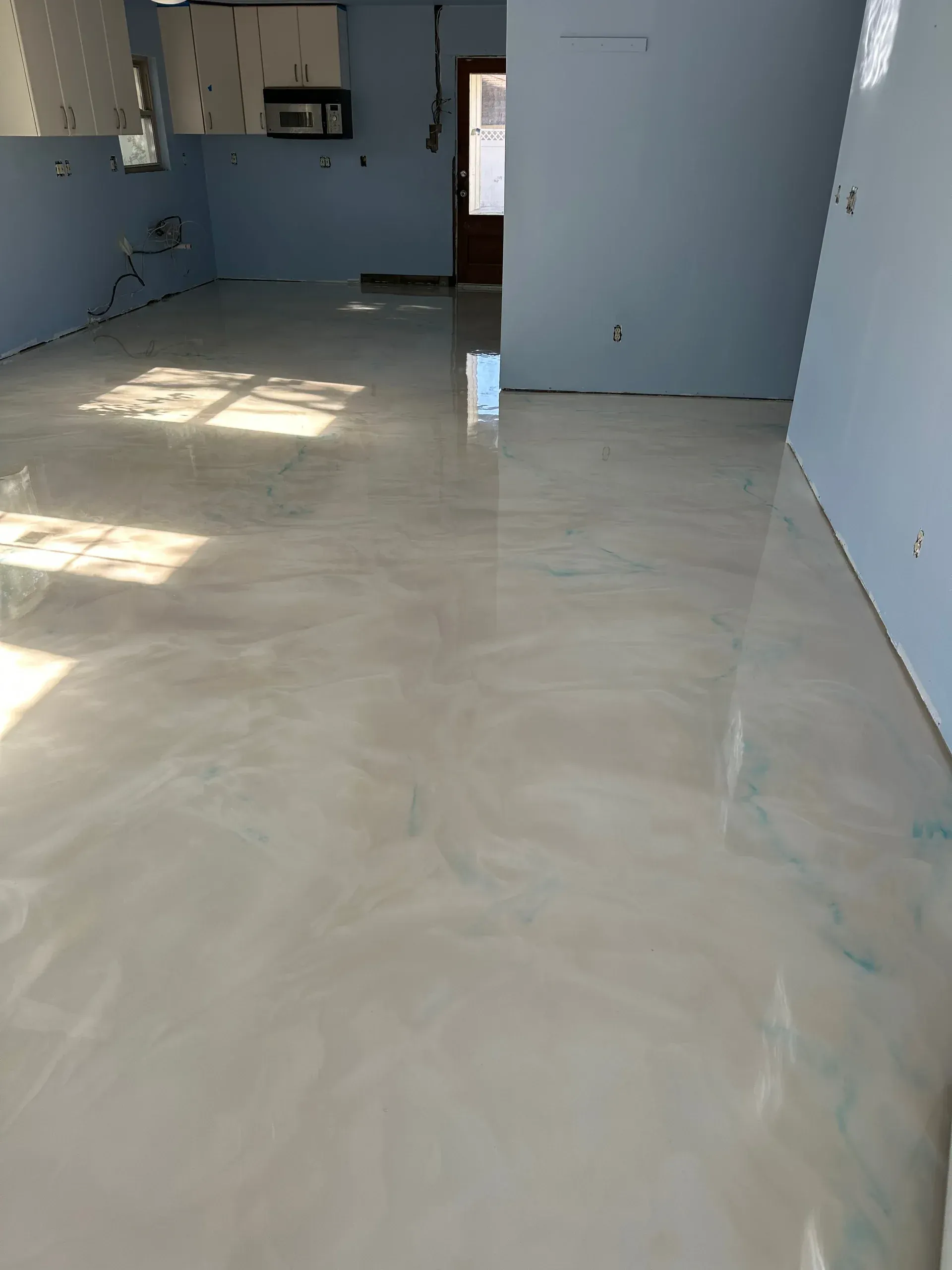 Shiny epoxy floor with light blue and white swirls in a room with blue walls and natural light.
