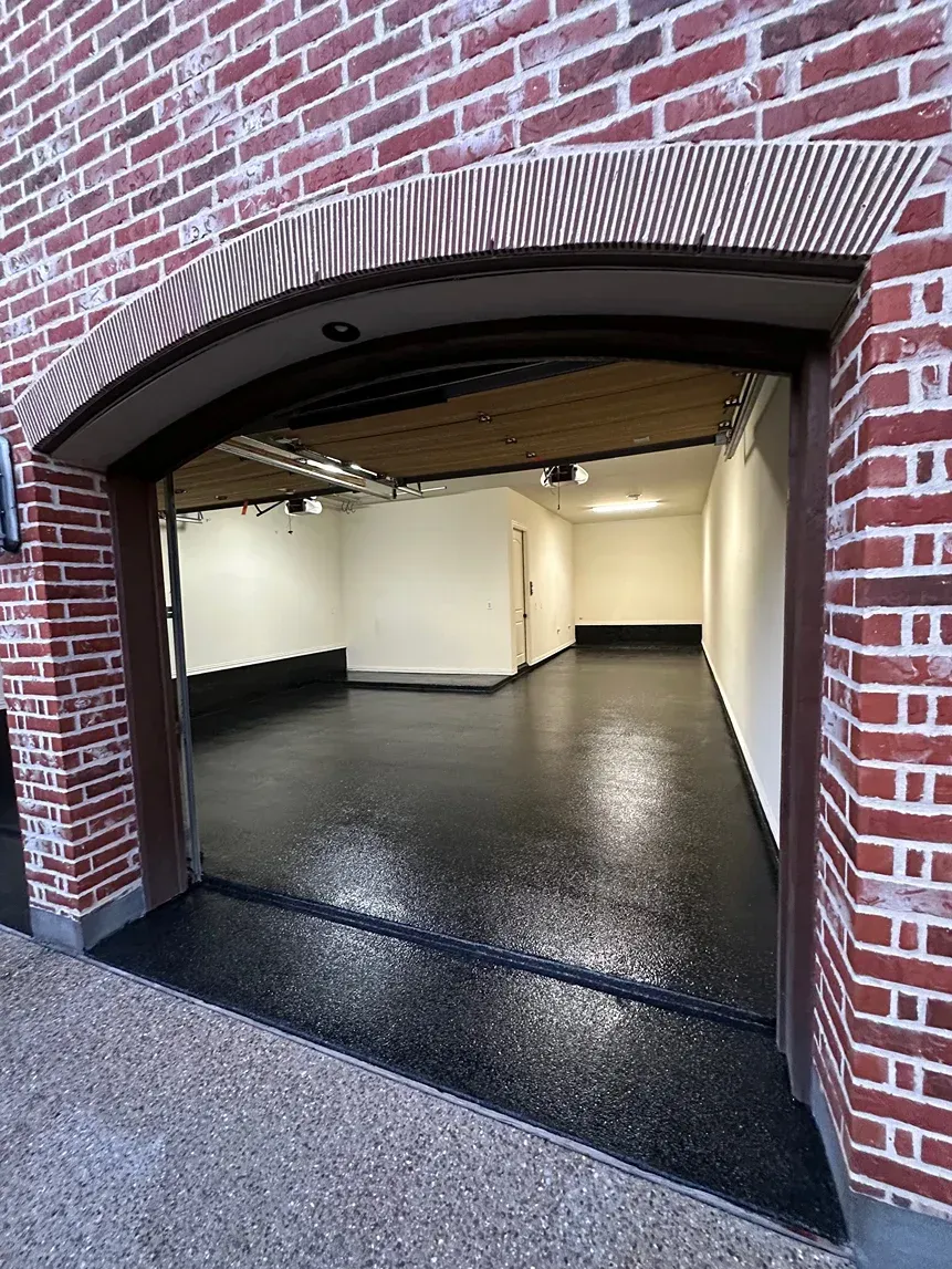 Open doorway of a brick building reveals a dark, glossy-floored room with white walls, and a wooden ceiling.