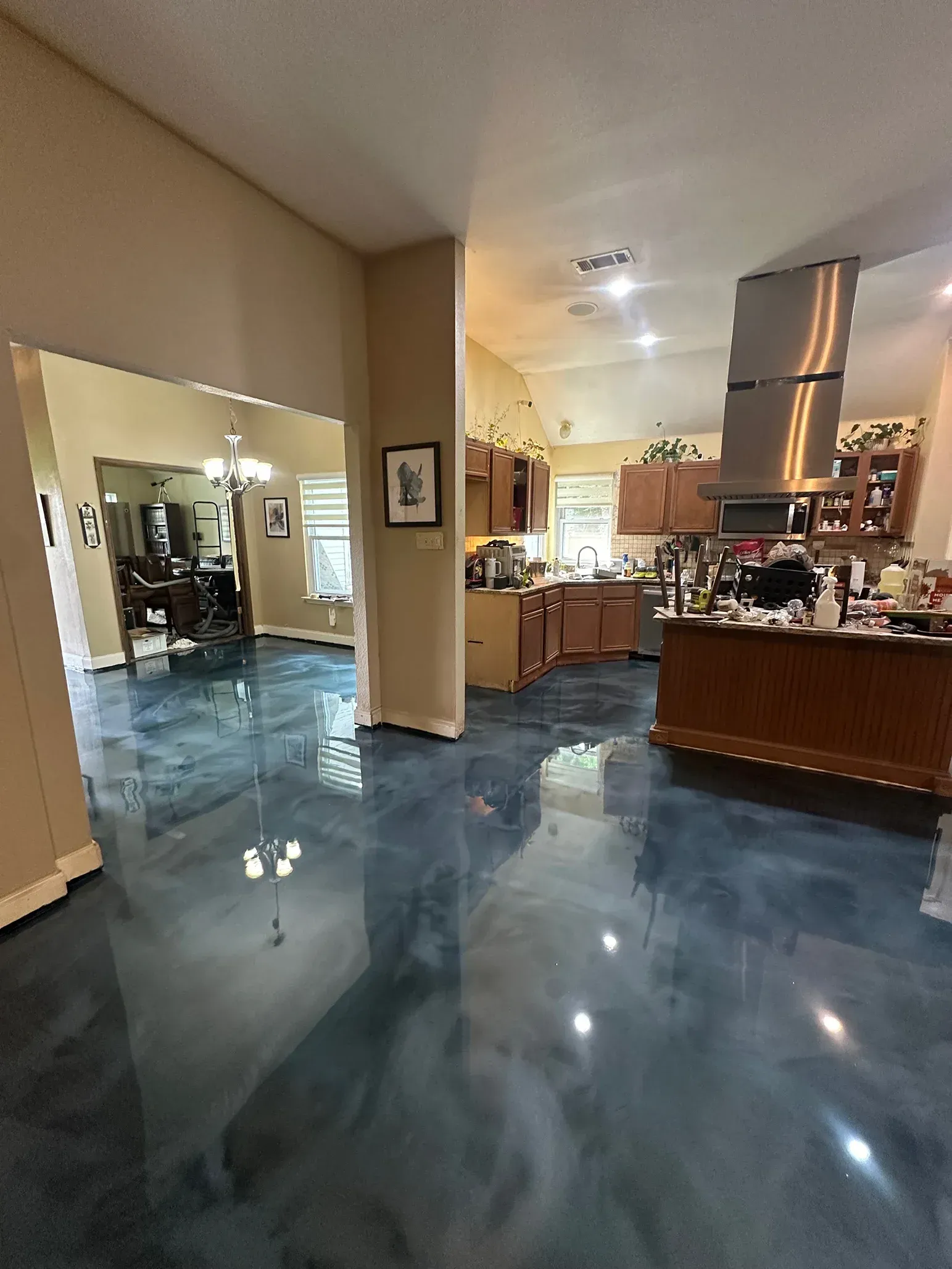 Open kitchen and living room with blue-gray epoxy floor and wooden cabinets.