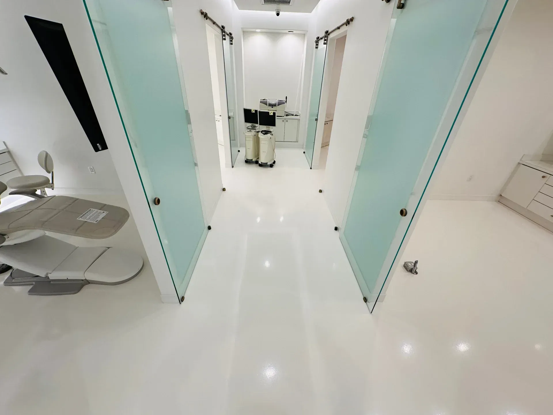White hallway with glass doors, medical equipment, and bright lighting.
