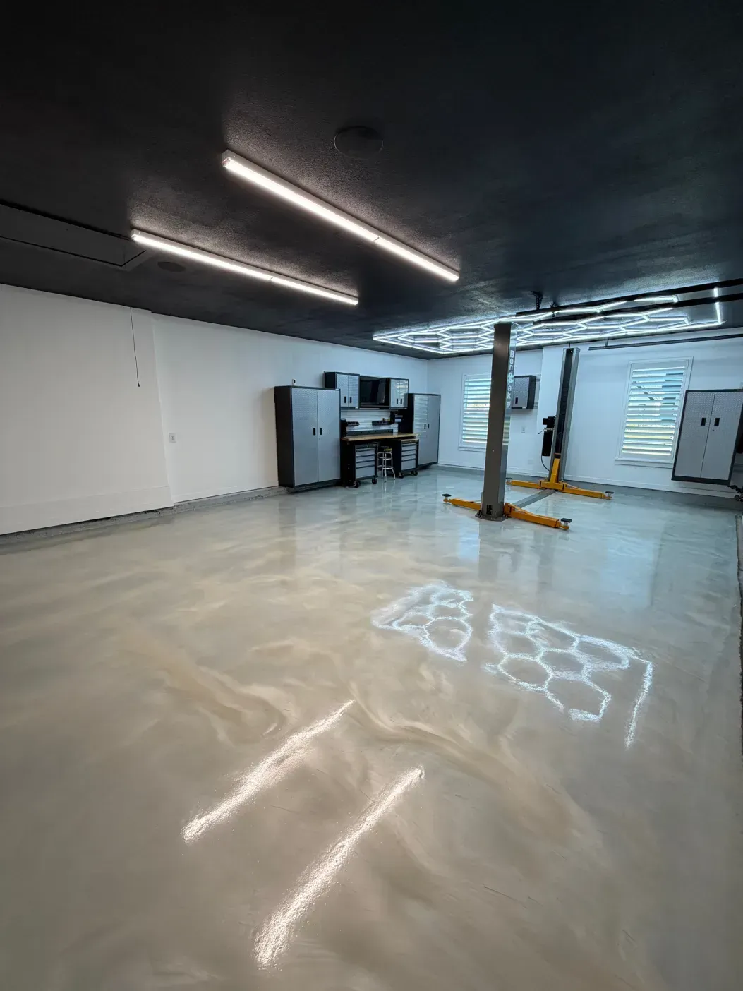 Garage interior with reflective epoxy floor, black ceiling, white walls, and a car lift.