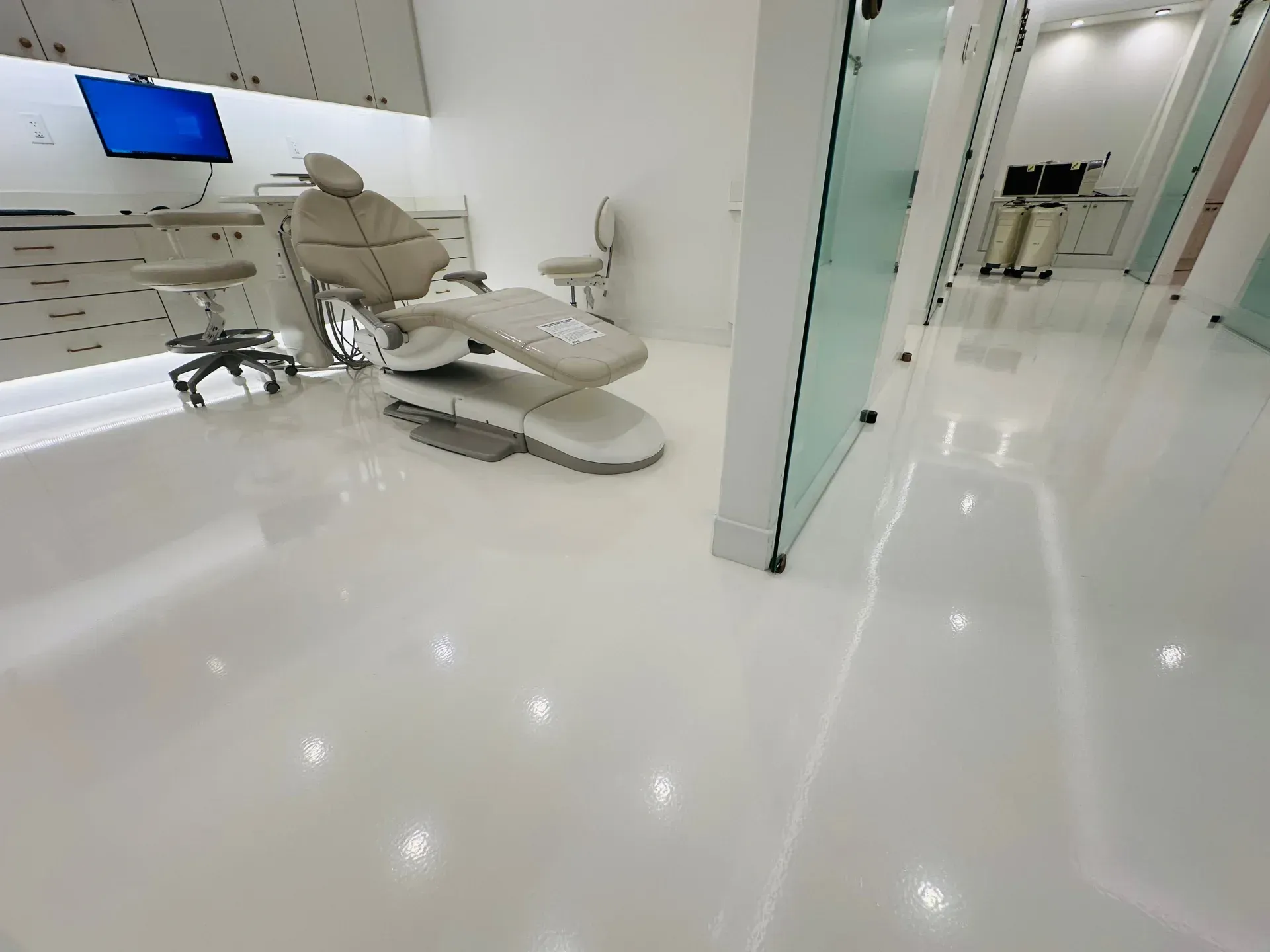 Bright, modern dental office with white flooring and walls. A dental chair and equipment are visible.