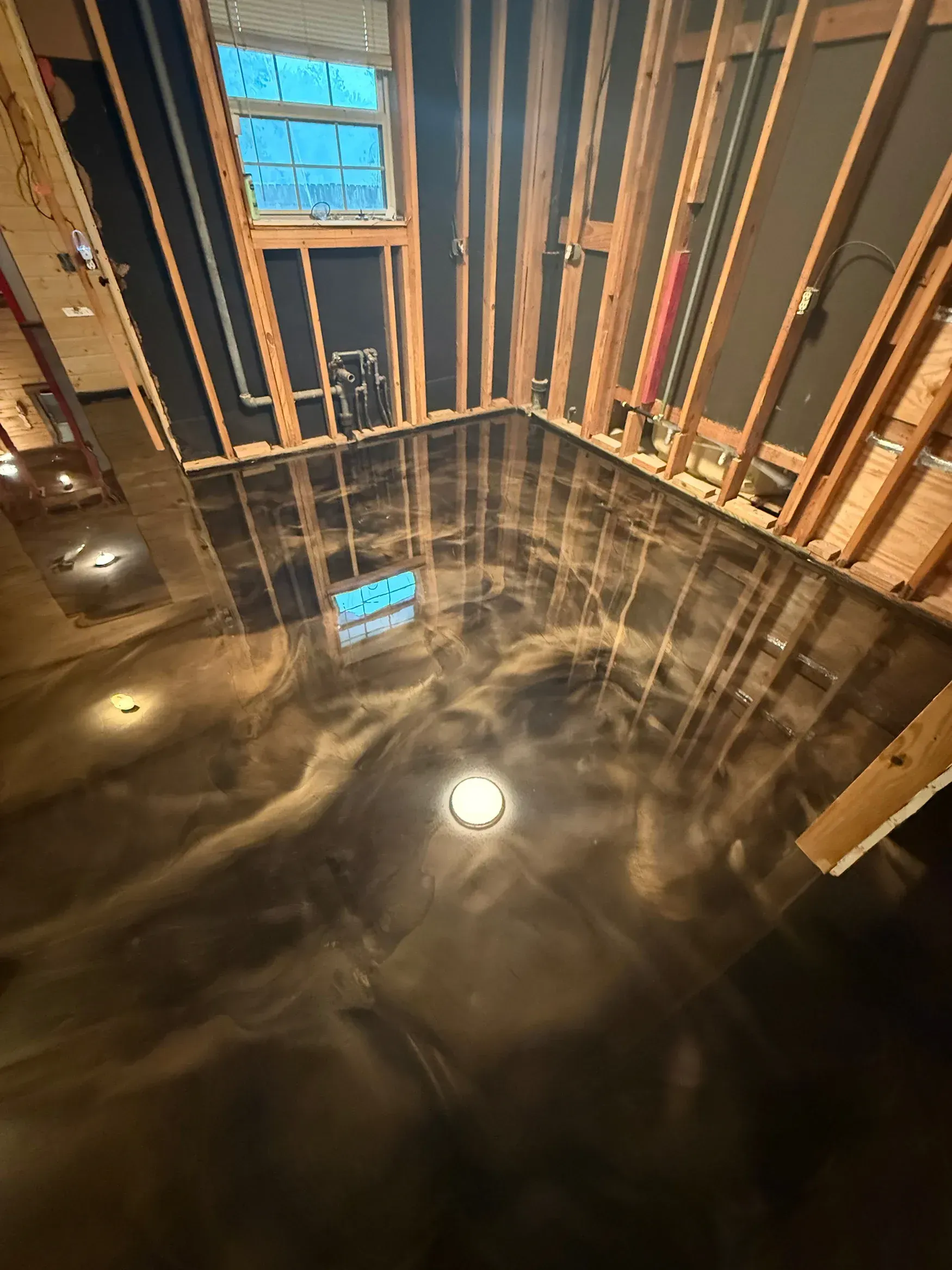 Metallic epoxy floor in an unfinished room, reflecting light. Wood framing on walls.