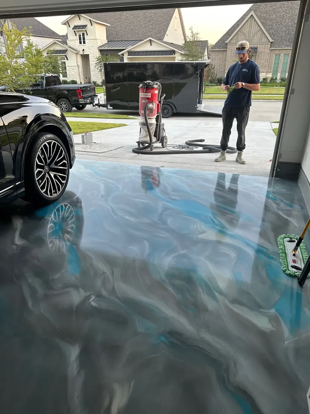 Garage with metallic blue-grey epoxy floor. Man stands near trailer, car parked inside.