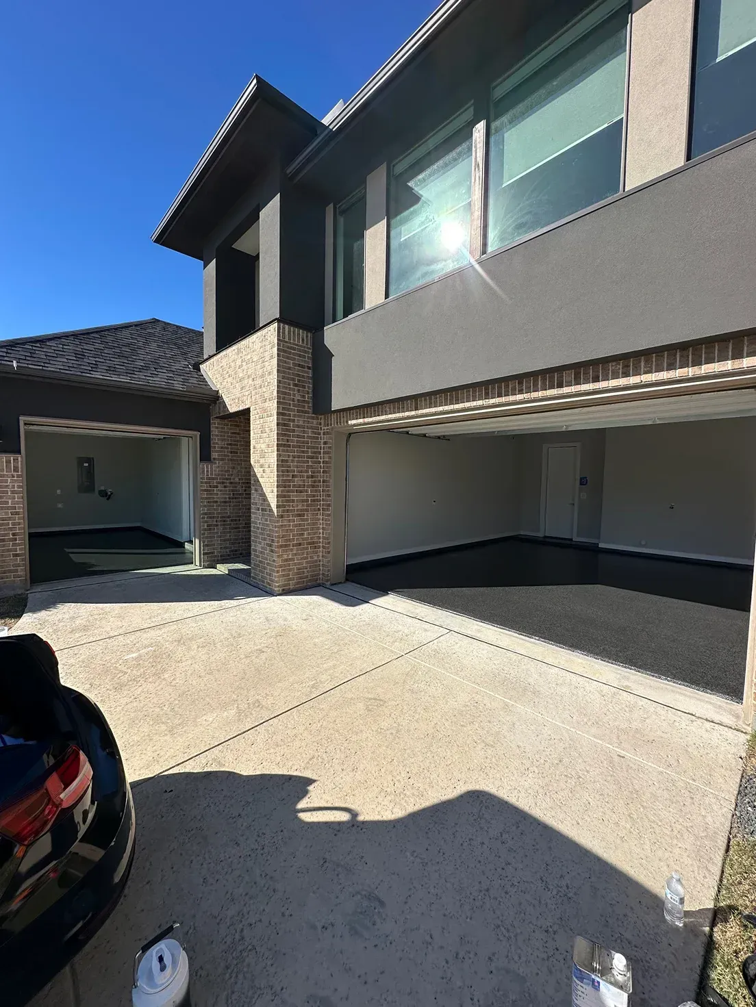 A modern house with open garage doors; sunny day. Concrete driveway, brick and dark facade.