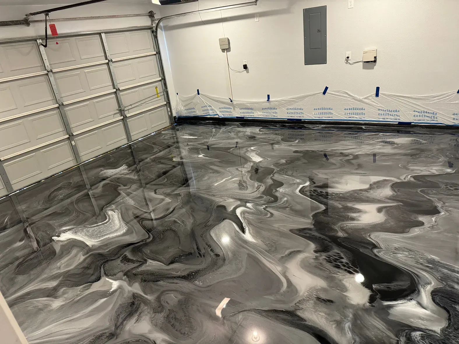 Garage with epoxy floor, swirling black, white, and gray colors. Garage door open.