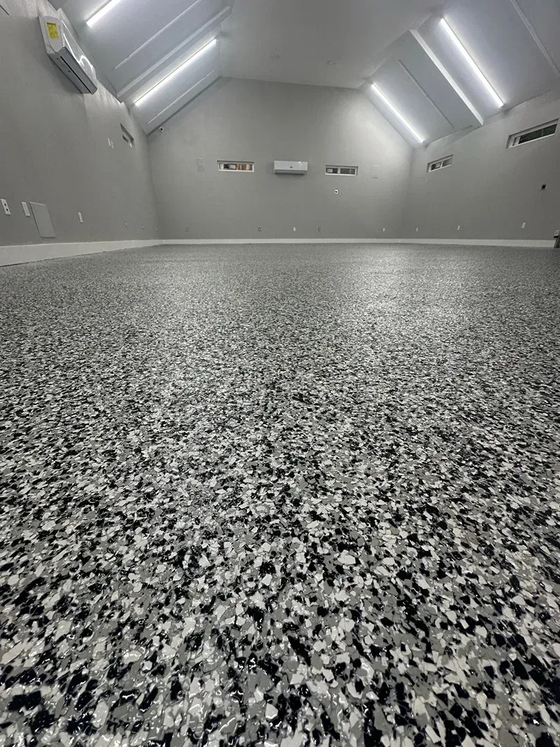 Grey and white speckled epoxy floor in a large, bright, empty room with a sloped ceiling and overhead lights.