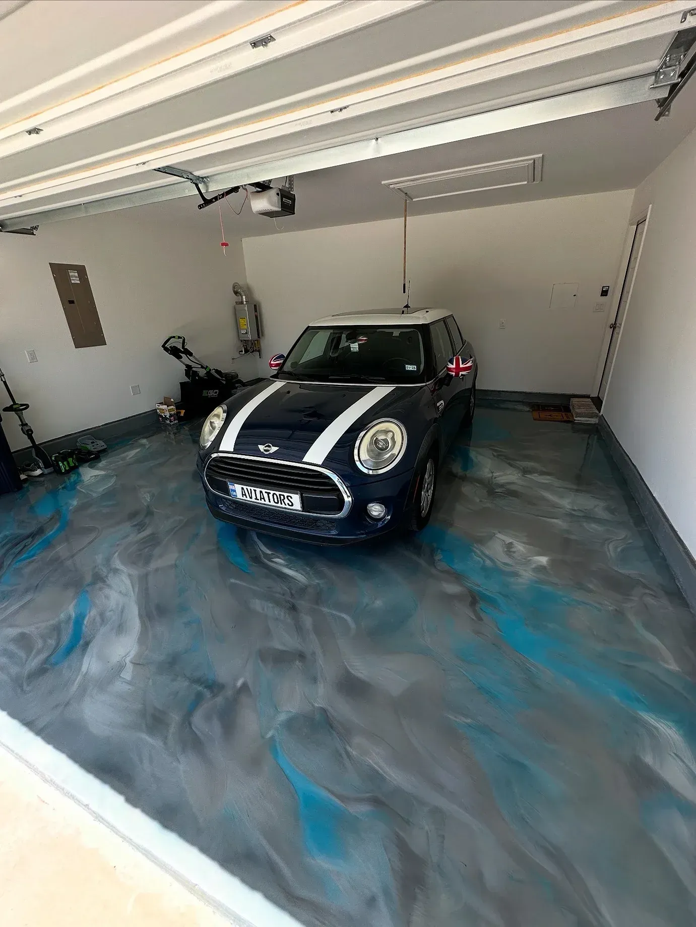 A blue Mini Cooper parked in a garage with a decorative, blue and gray epoxy floor.