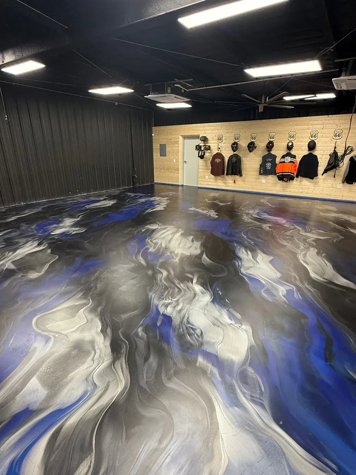 Swirled blue, silver, and black epoxy floor in a room with black ceiling, clothes hanging on the wall.