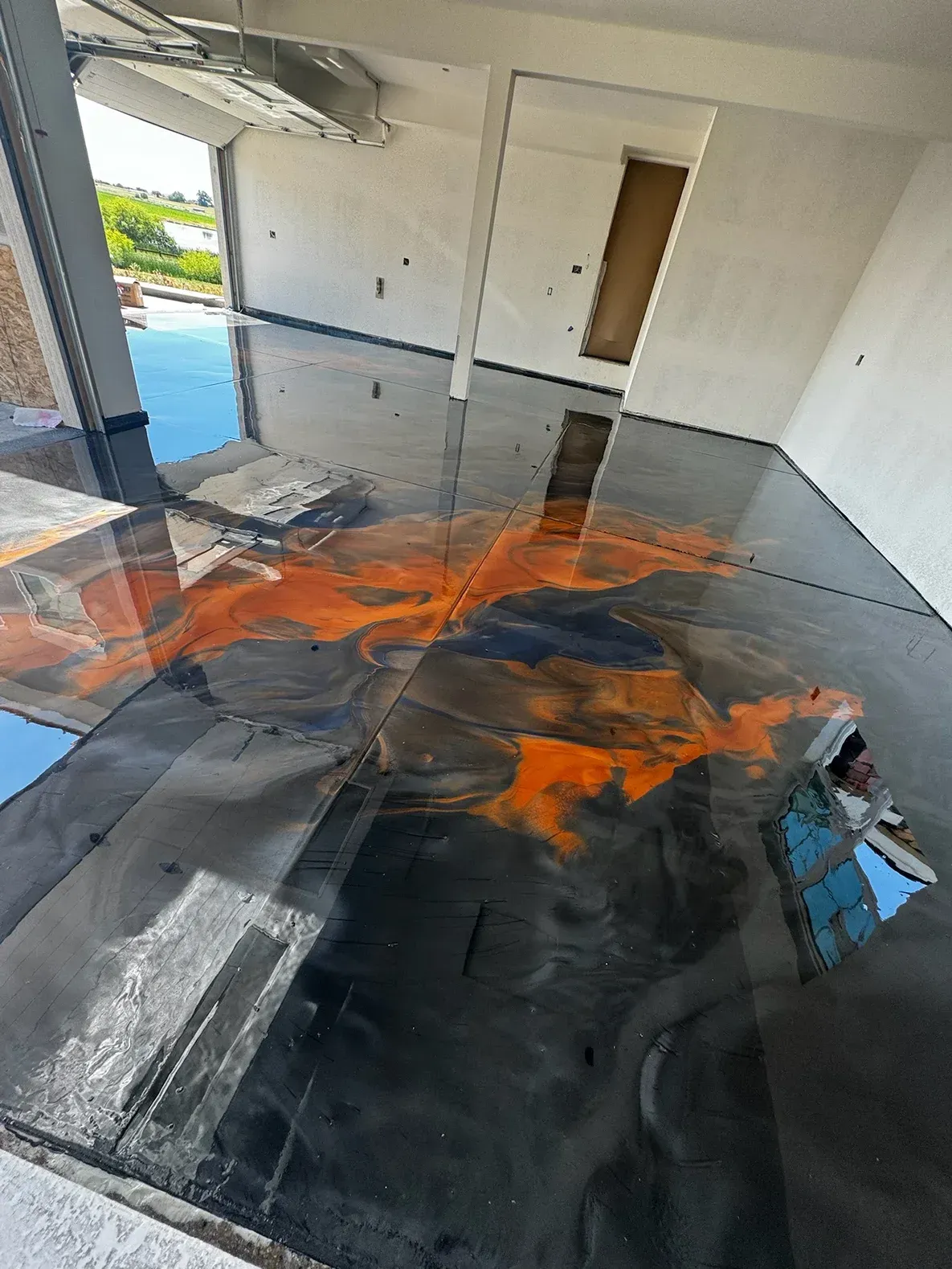 Metallic epoxy floor with orange and black swirls in an unfinished room.