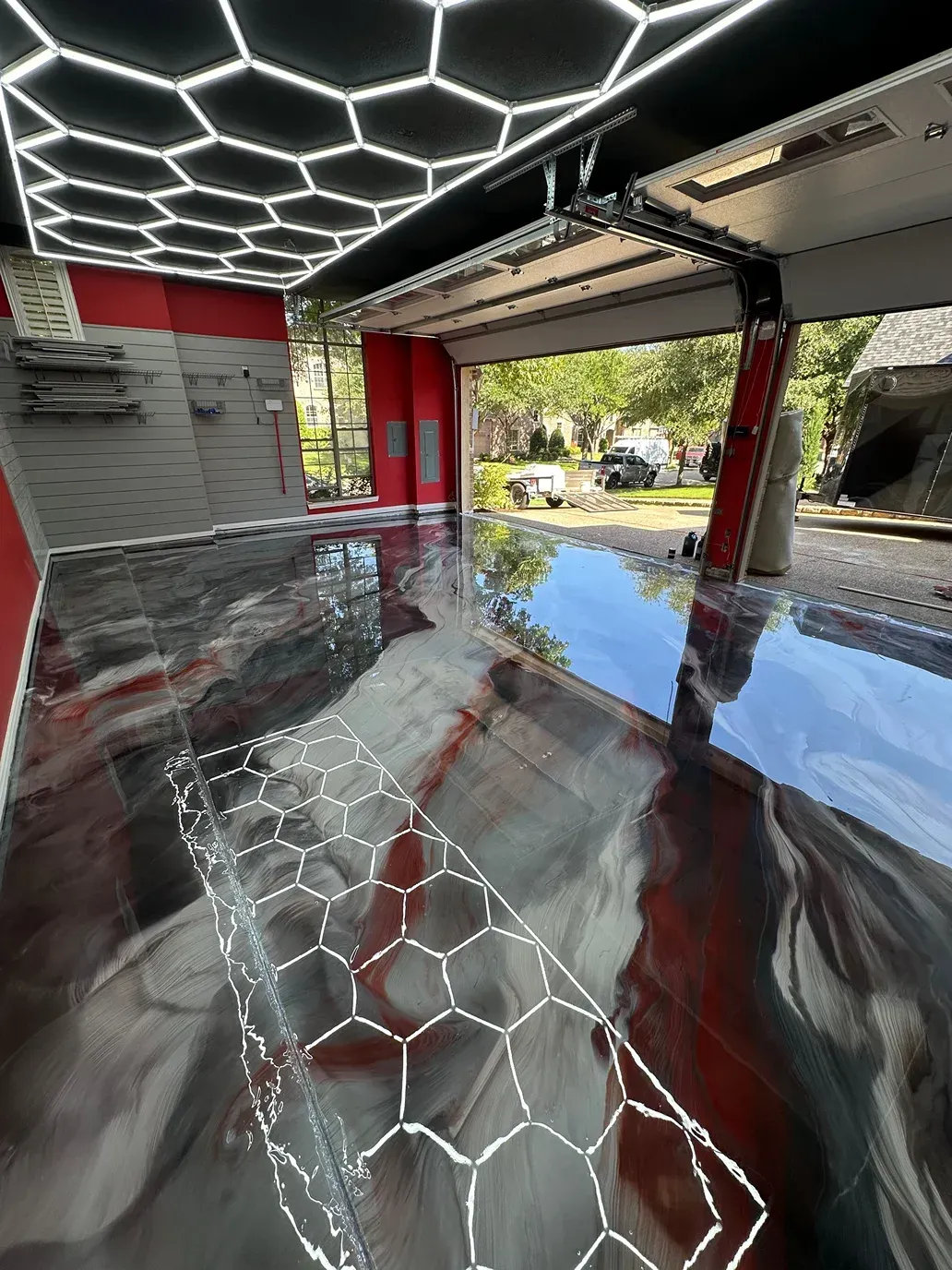 Garage interior with glossy epoxy floor, honeycomb ceiling, and open garage door.