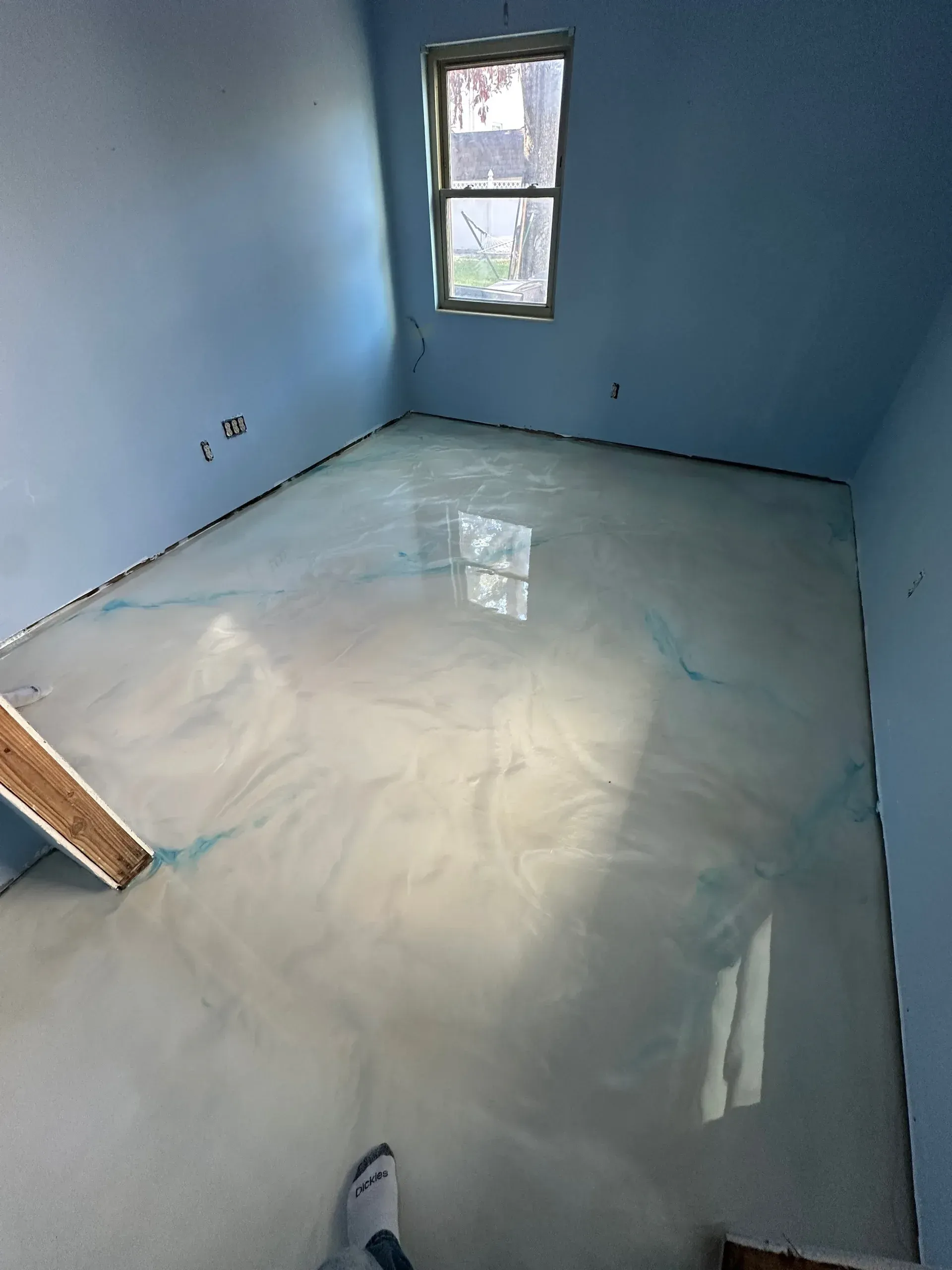 Room with shiny, light-colored epoxy floor and light blue walls. A window is visible.