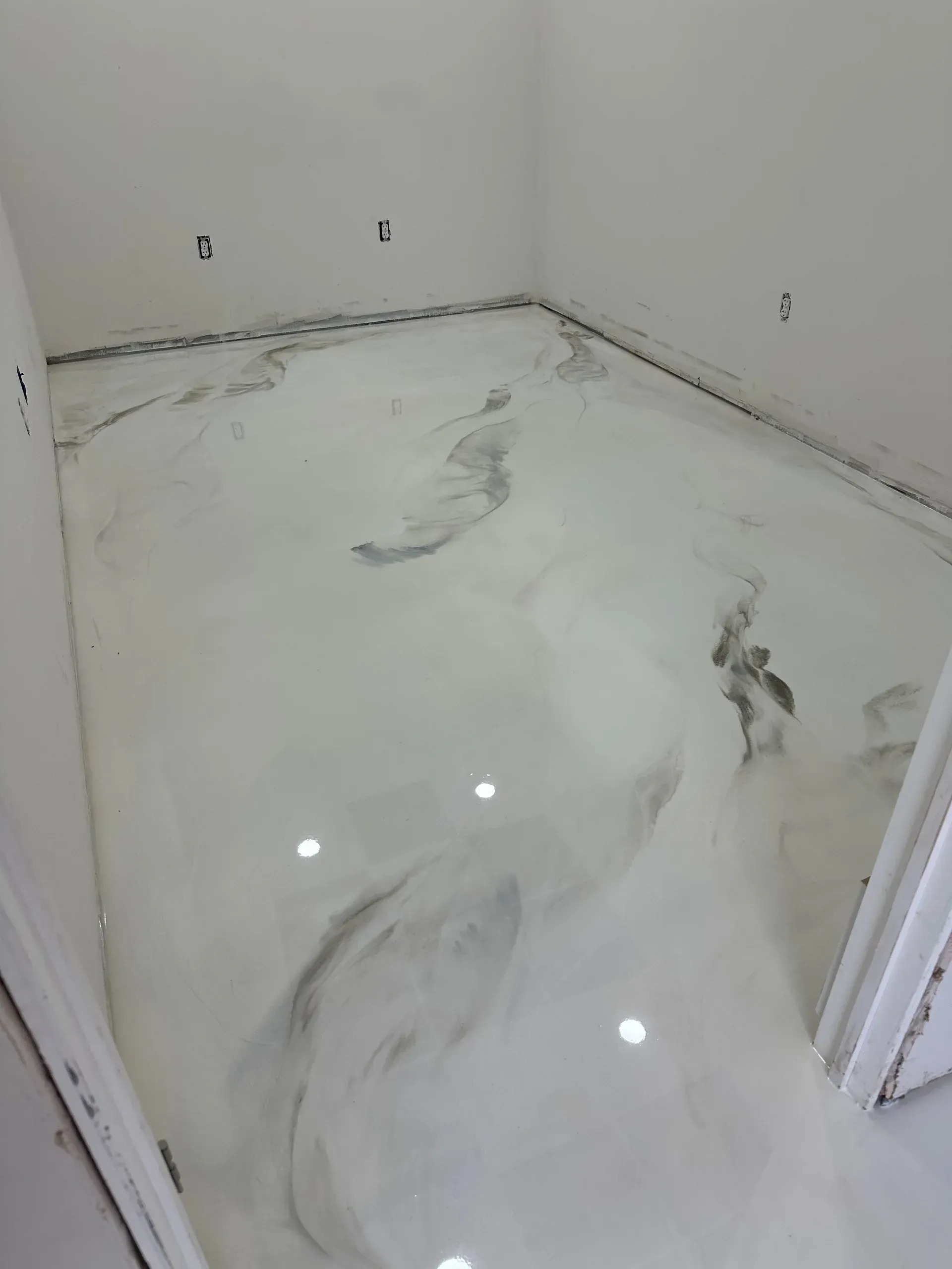 Room with glossy white epoxy floor, marble effect, with dark gray swirls.  Empty space, white walls, and some outlets.