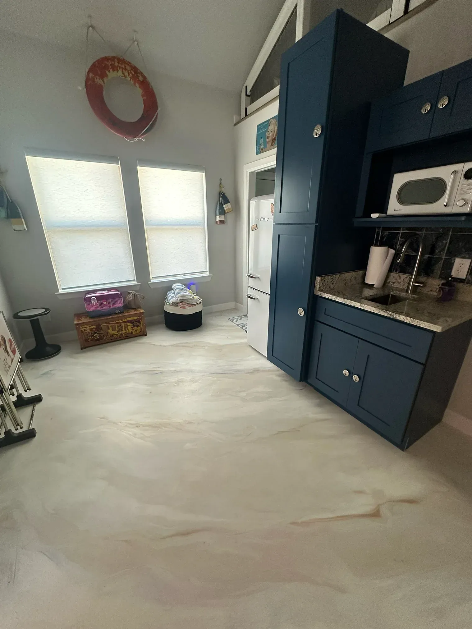 Small kitchen with blue cabinets, a microwave, and a white refrigerator; windows with blinds and a life preserver.