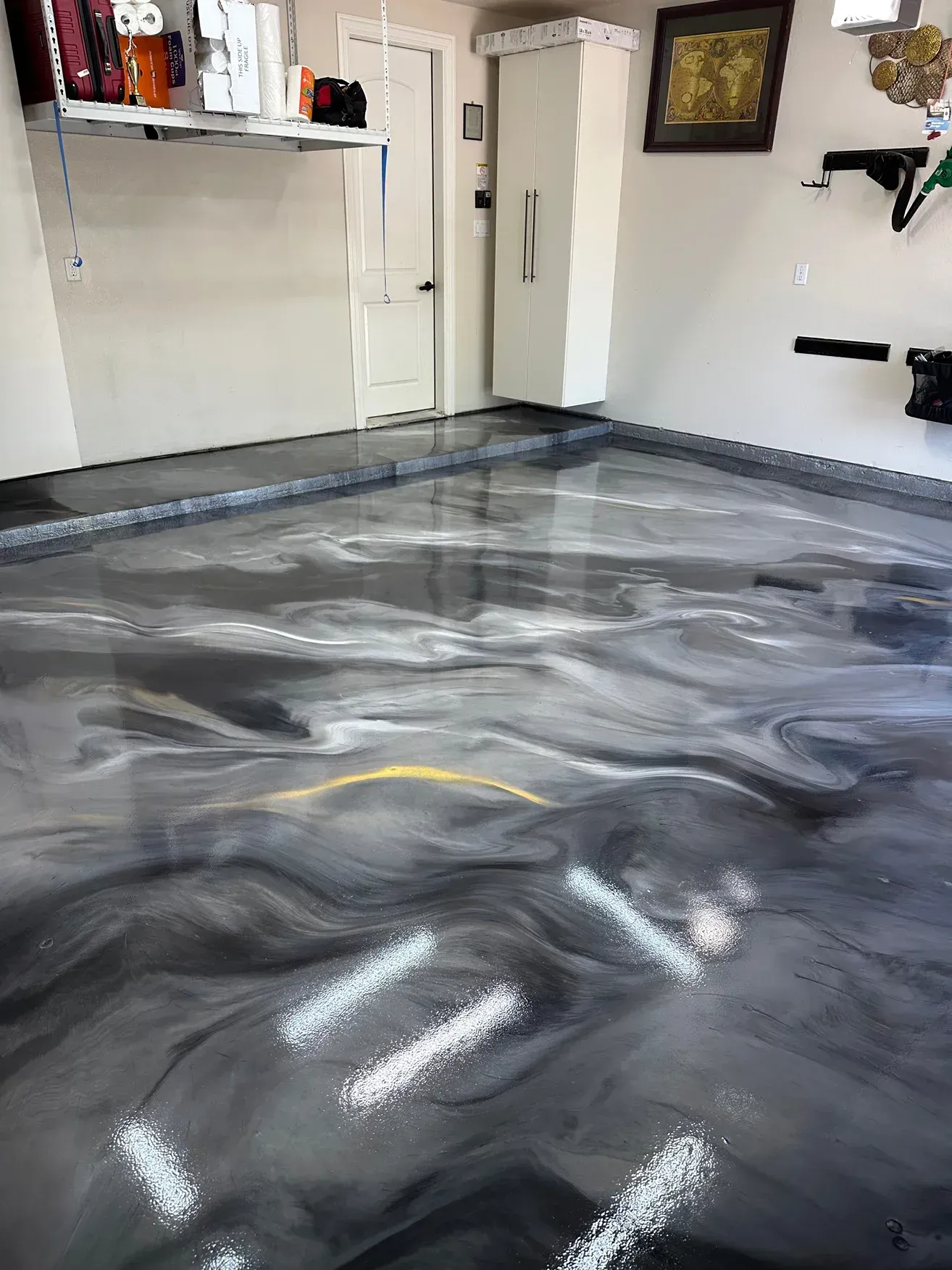 Garage floor with a shiny, swirled epoxy finish in shades of gray, black, and white.