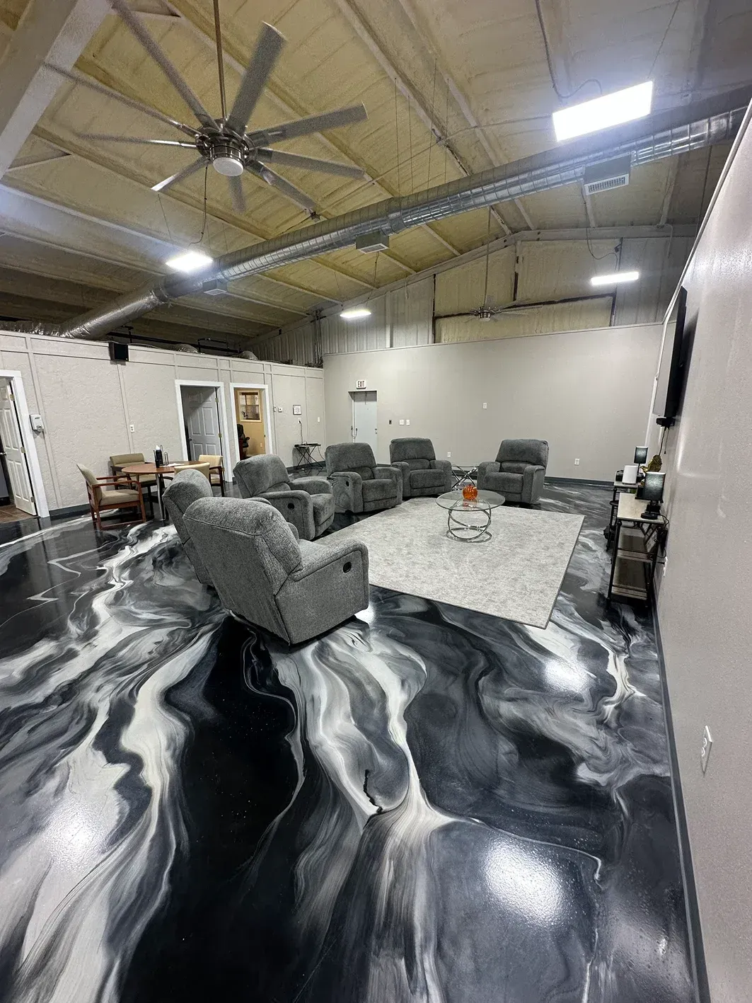 Large room with black, white, and gray swirled epoxy floor. Recliners, rug, coffee table, and ceiling fan are visible.