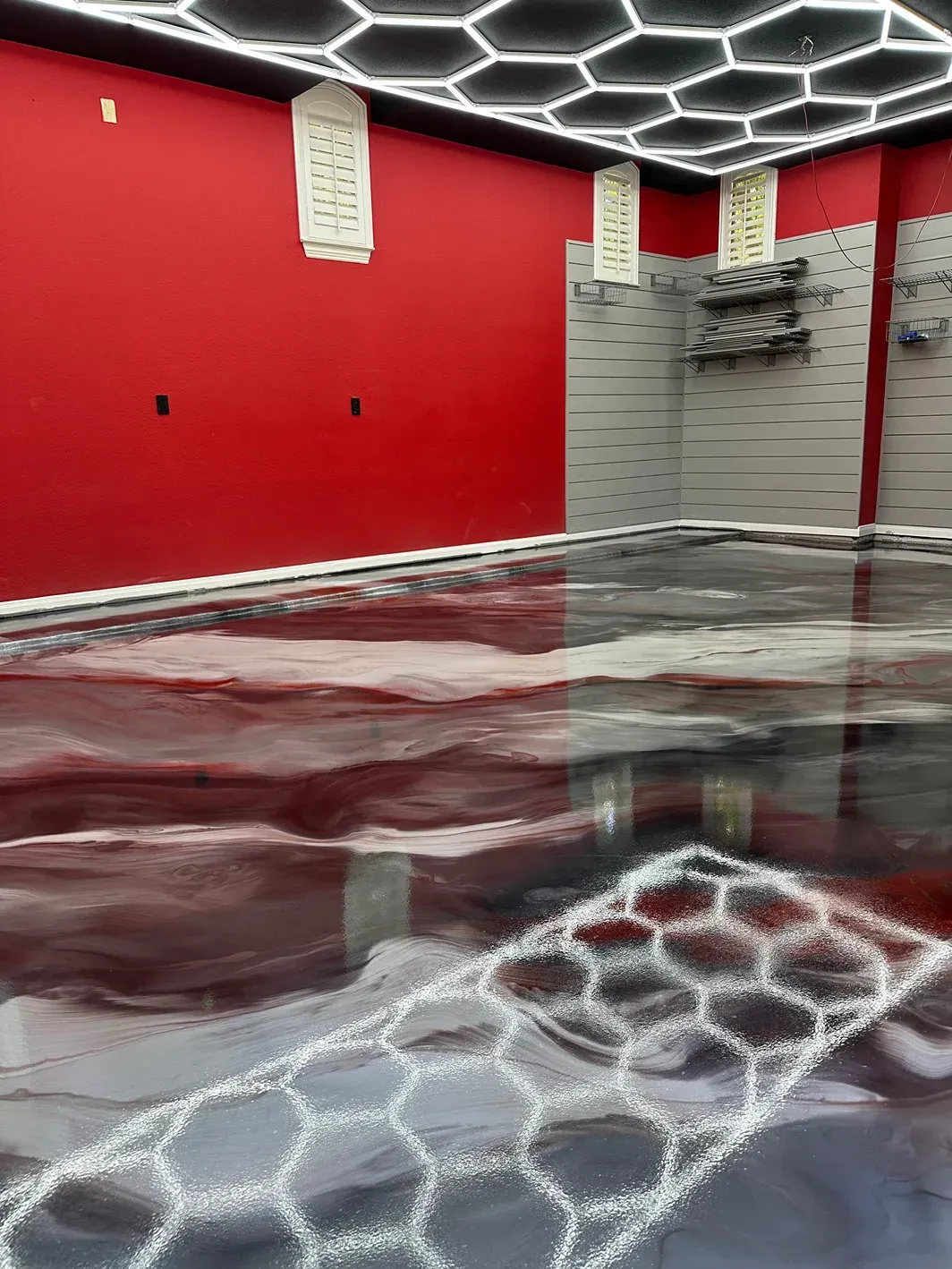 Room with red walls, gray and burgundy reflective floor, honeycomb ceiling lights.