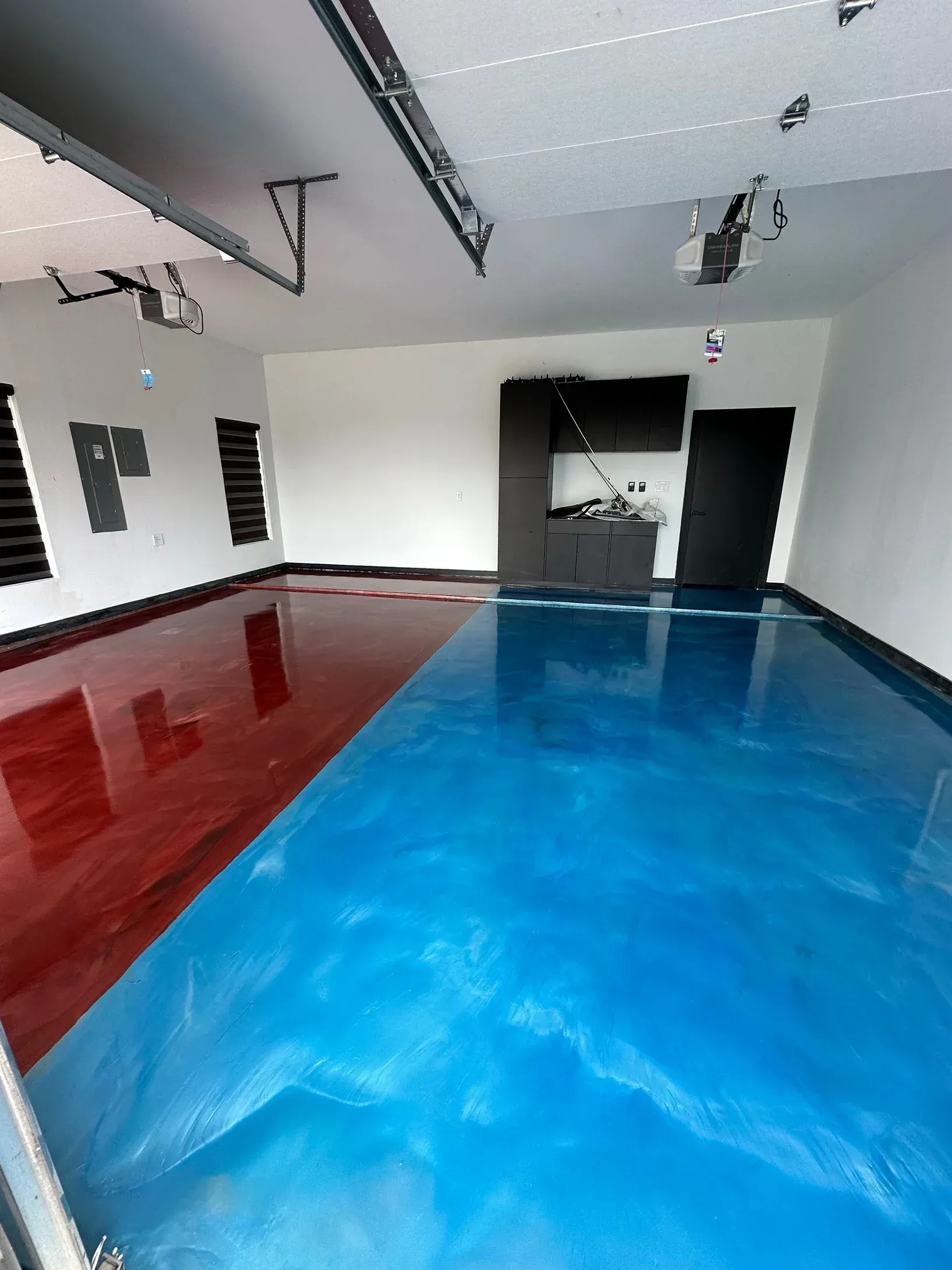 Garage interior with a blue and red epoxy floor, white walls, and dark cabinetry.