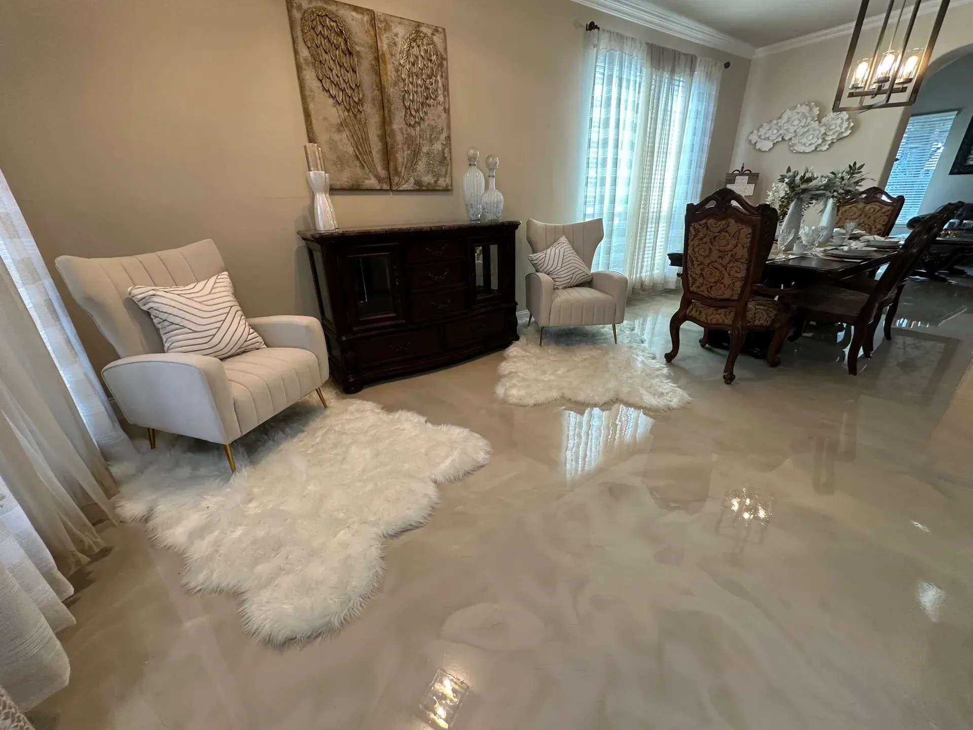 Living room with light-colored furniture, white rugs, and a dining area, featuring a reflective, metallic floor.