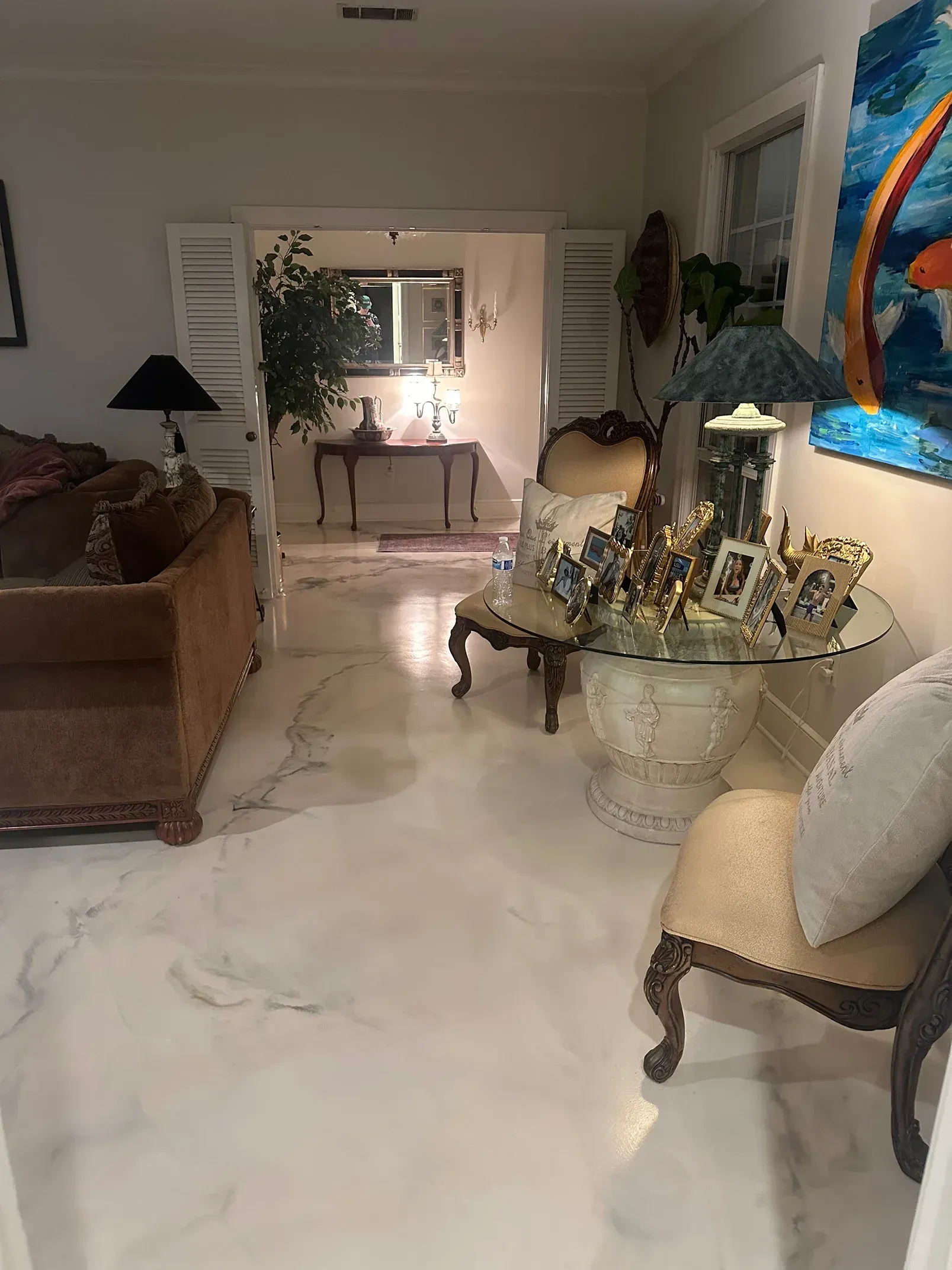 Living room with white marble floor, ornate chairs, sofa, and view into an entryway with a table and mirror.