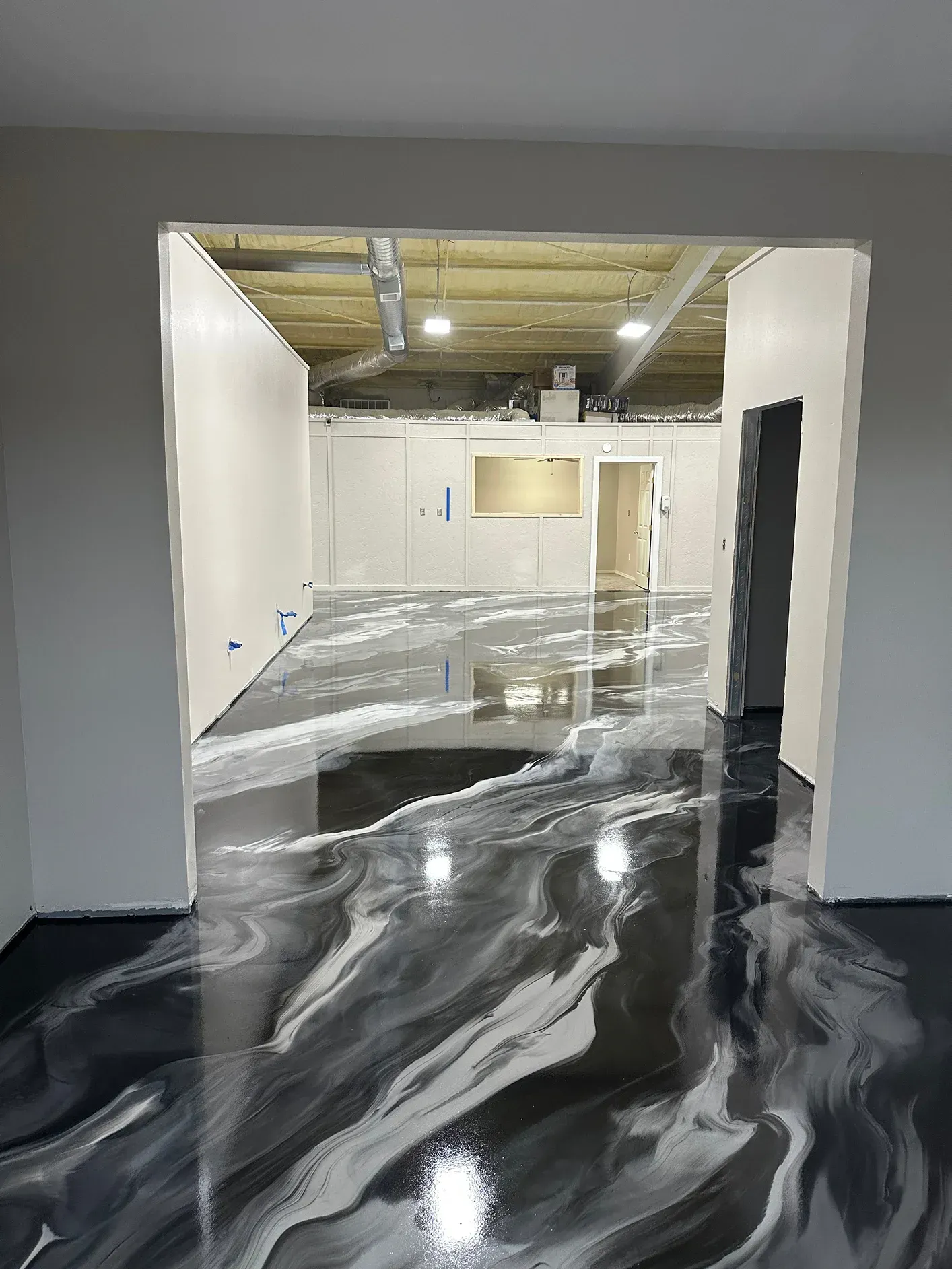 Epoxy-coated floor in shades of gray, white, and black with a glossy finish, viewed through a doorway.
