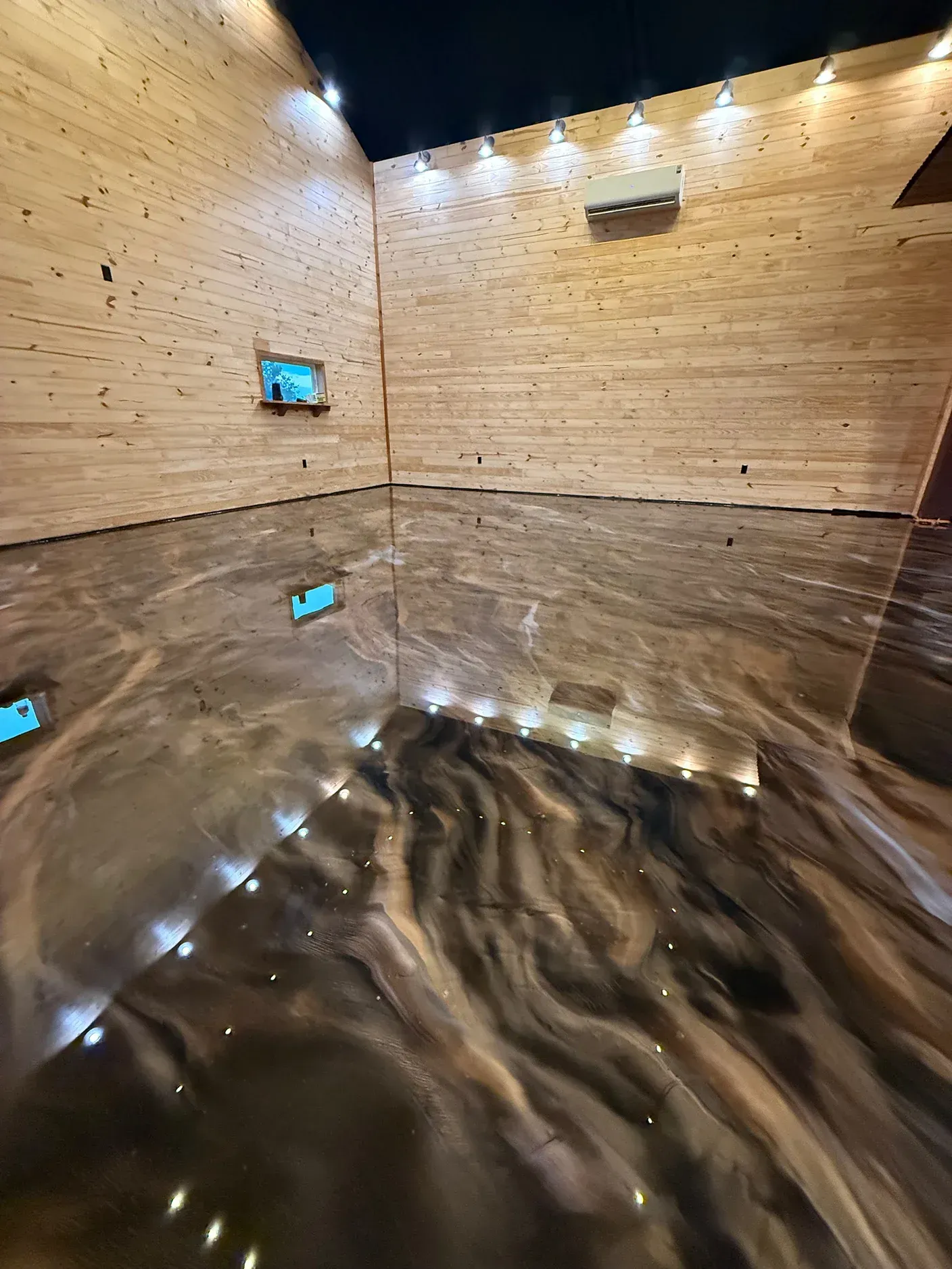 Wooden-walled room with a shiny, metallic-looking floor reflecting the lights above.