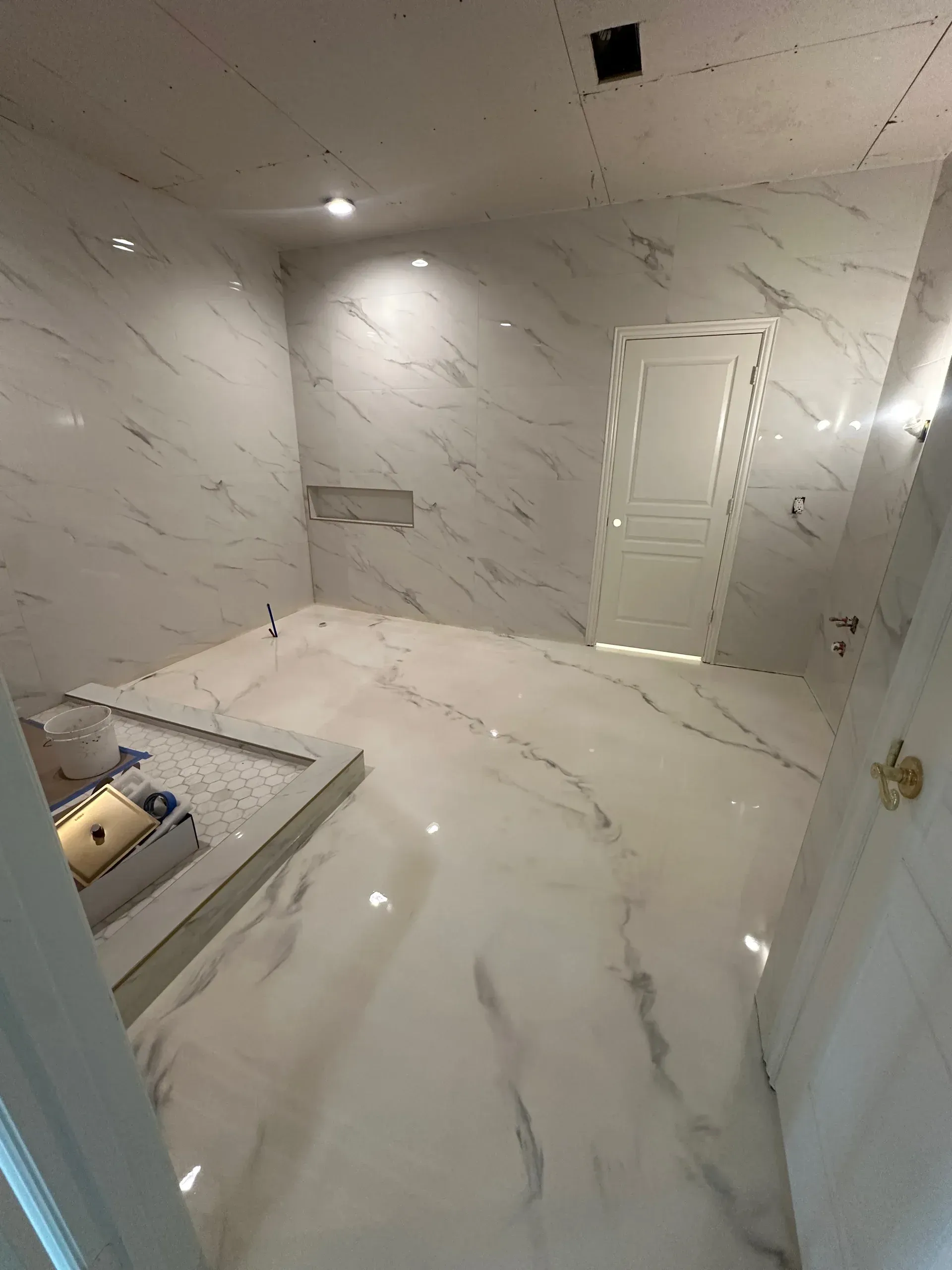 White marble bathroom with door, recessed lighting, and built-in tub area.