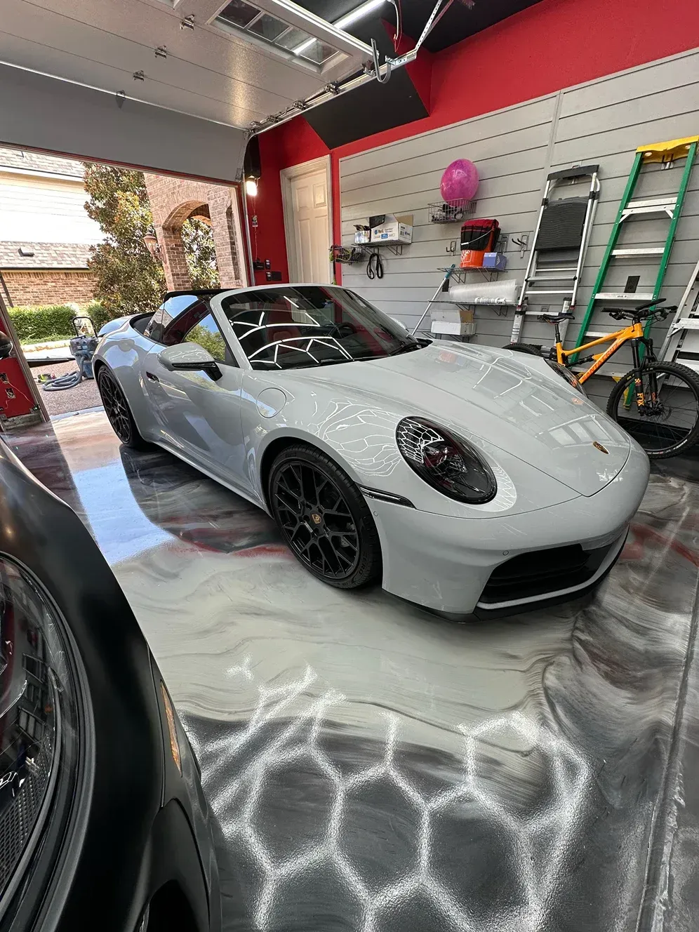 Light gray convertible Porsche in a garage with reflective epoxy floor.