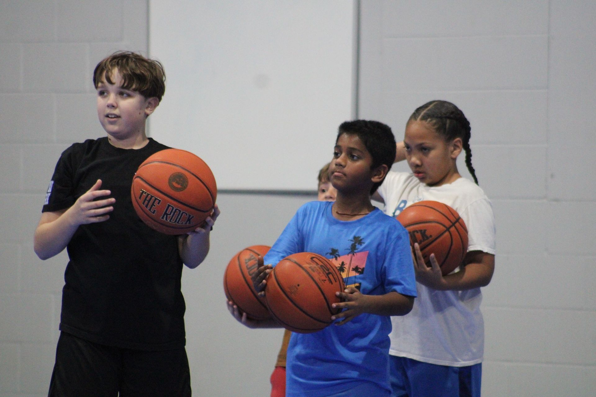 Three children standing in an indoor gym, each holding a basketball.
