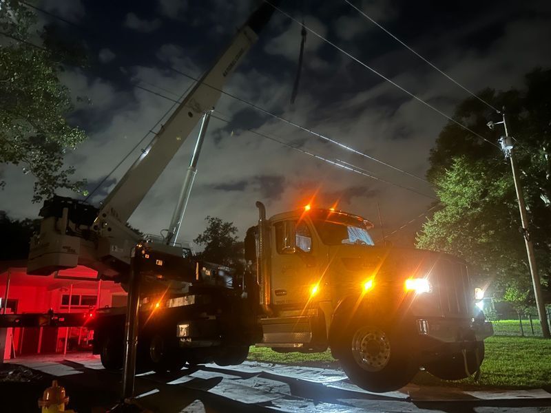 A utility truck with its crane extended, working on power lines at night. The truck has flashing lights.