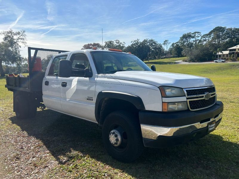 White Chevrolet Silverado truck with a flatbed, parked on grass in a sunny outdoor setting.
