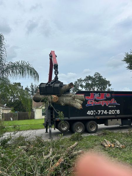 A truck with a crane loading tree branches. The truck, from J&J's Stumpage, is black with a logo.
