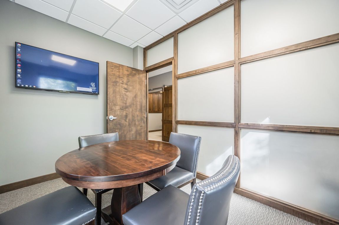 A conference room with a round table and chairs and a flat screen tv