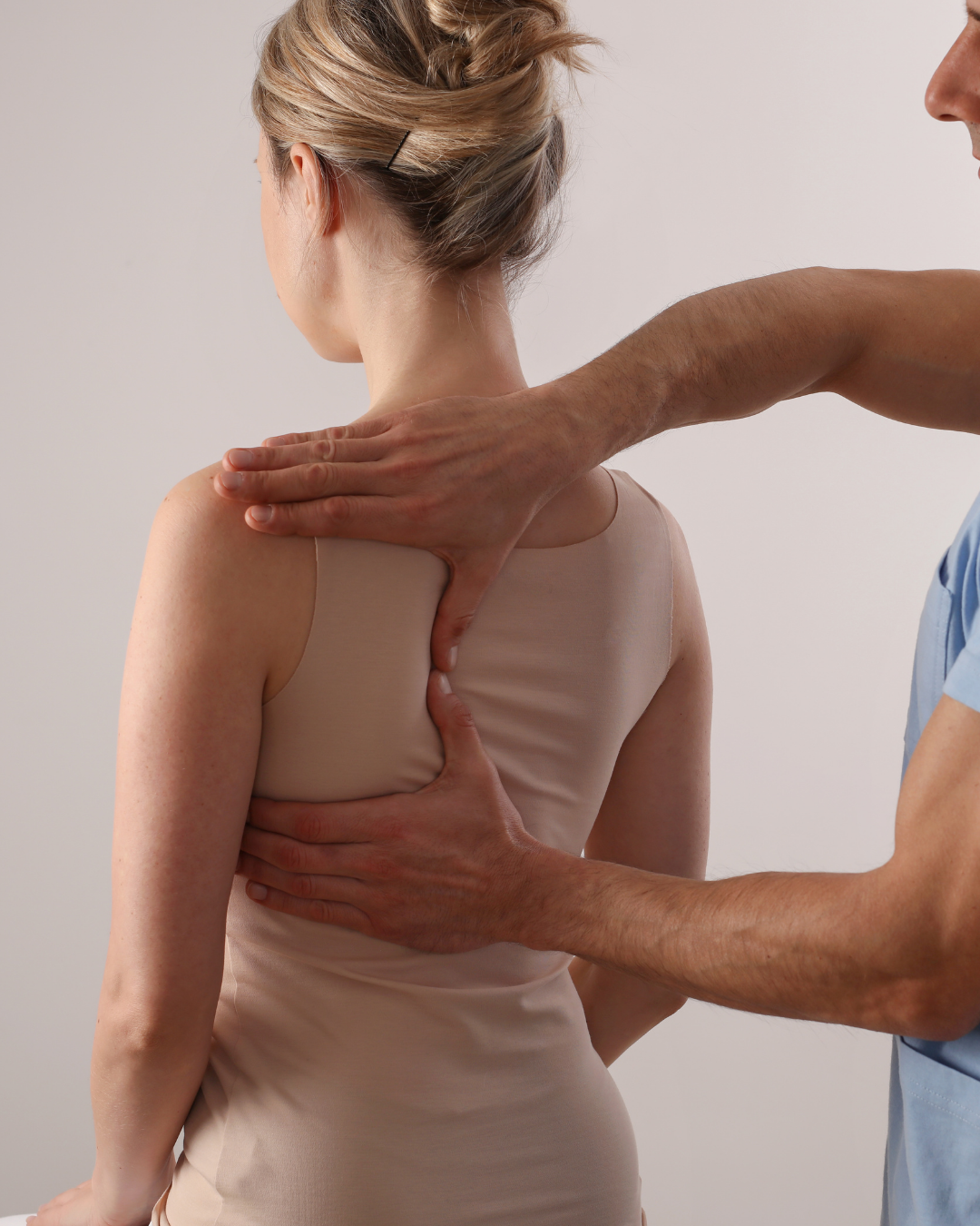 A healthcare professional examines a woman's back, pressing with hands near her shoulder blades.