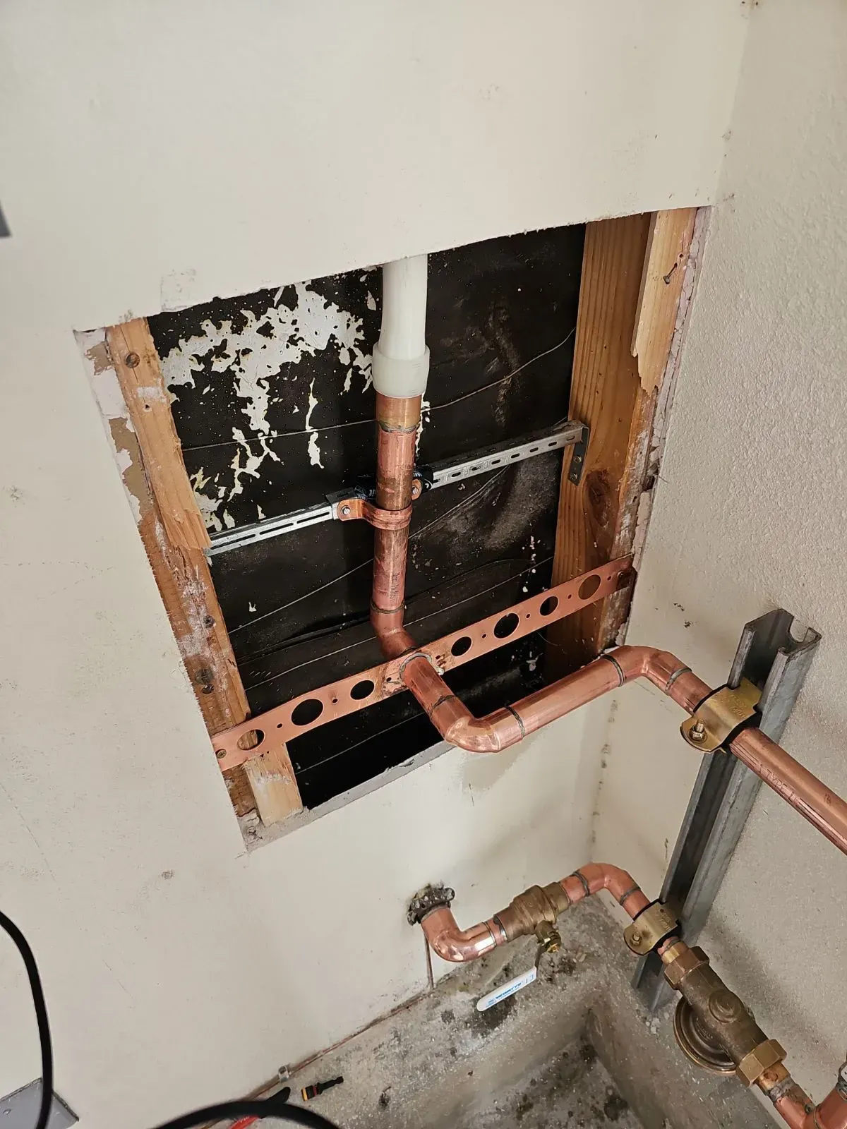 Copper pipes exposed within a wall cavity, likely for plumbing repairs. The pipes are brown, against a black backdrop.