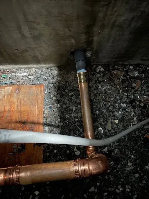 Copper pipes and fittings emerging from a wall with a black plastic pipe. A cable runs across the pipes.