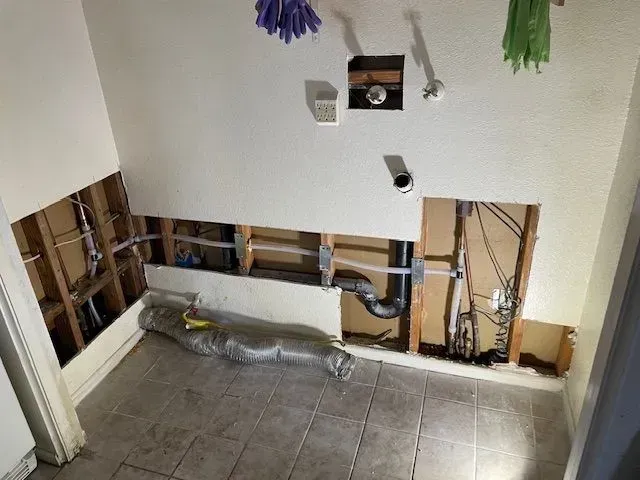 Bathroom renovation in progress; exposed plumbing and wiring in walls, tile floor, and open drywall.