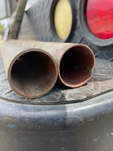 Two cylindrical metal pipes with open ends, resting on a textured black surface near a vehicle's red tail light.