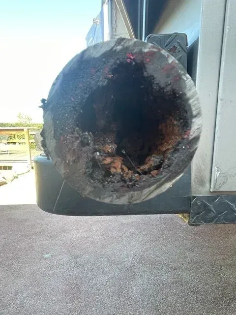 Severely damaged pipe with a charred, hollow interior against a gray metallic surface. The setting appears outdoors.