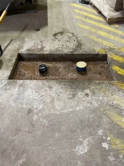 A rectangular concrete trench with two circular objects inside, in an industrial setting. The floor has yellow and black safety markings.