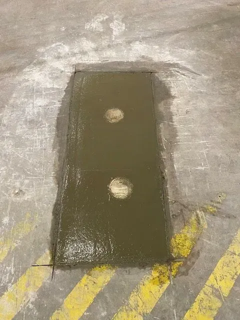A rectangular floor depression filled with liquid, containing two circular holes. Located in a warehouse or industrial space with yellow hazard stripes.