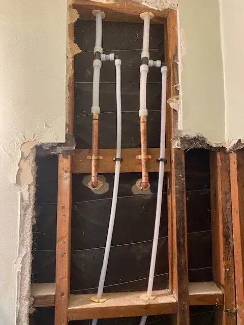 Plumbing pipes and fittings installed in a wall cavity, showing copper and plastic pipes. The wall is opened during construction.