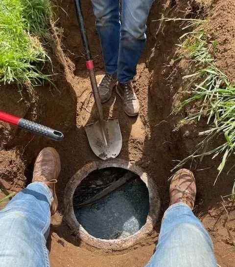 People excavating around a concrete septic tank in a grassy area. One holds a shovel.