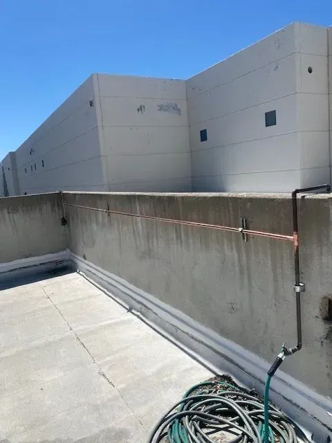 Rooftop with a concrete wall, a building in the background, and a green hose. Copper wire runs along the wall's top.