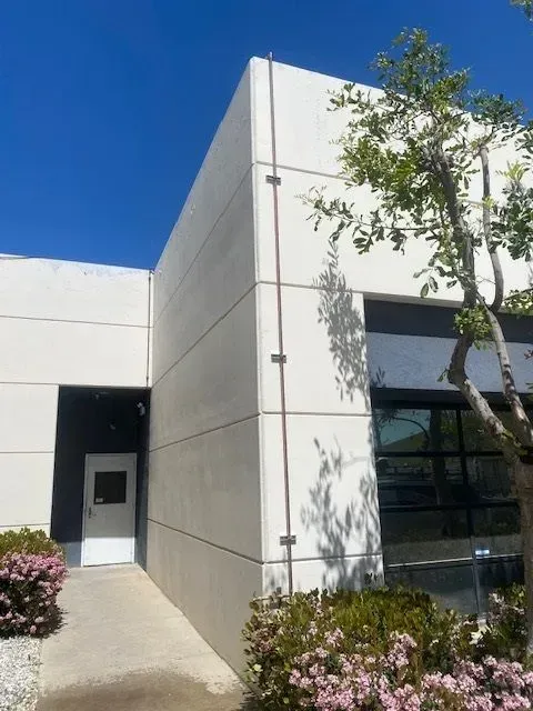 Exterior view of a modern building with light-colored walls and a dark blue sky. Brown rods run vertically along the building's corners.