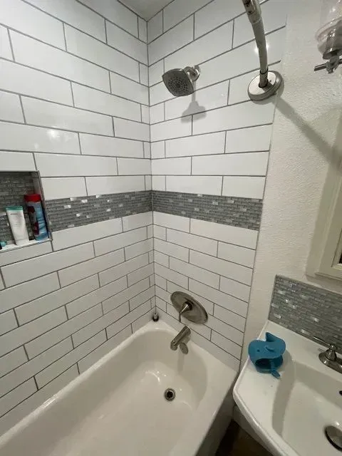Small bathroom with white subway tile shower and gray accent band. A white bathtub, sink, and chrome fixtures are present.