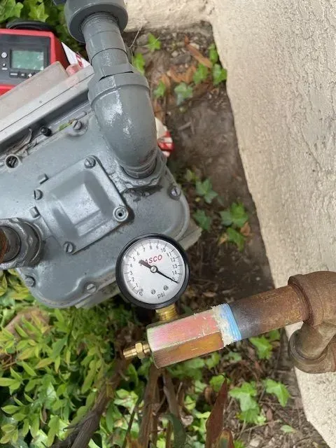 A close-up shows a gas meter with a pressure gauge attached, likely for testing. The meter is gray, the gauge black and white.