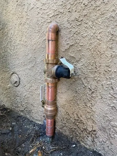 A copper pipe assembly with a valve attached to a stucco wall, likely an outdoor water shut-off.