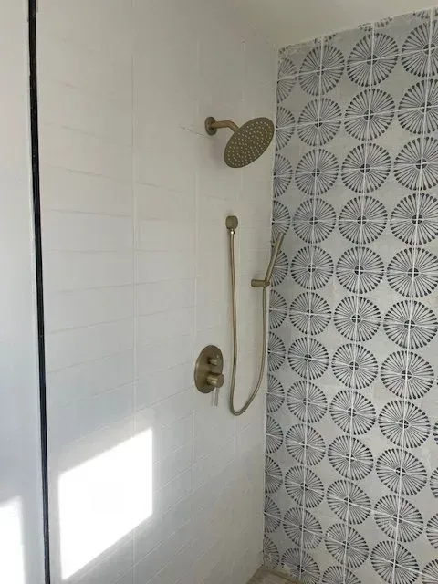 Shower with gold fixtures and patterned blue and white tile accent wall. White tile lines the other wall.