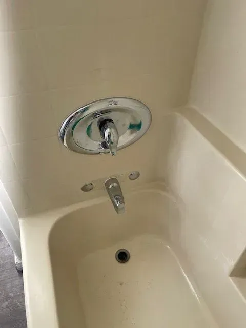 Beige bathtub and shower fixture with a chrome faucet and handle against a matching wall.